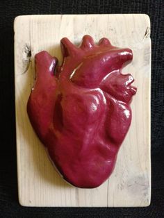 a red heart shaped object sitting on top of a wooden board