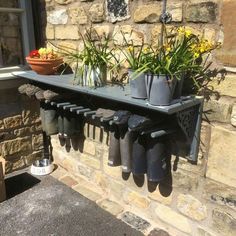 a shelf with some flowers and rain boots hanging from it's sides on the side of a brick building