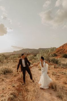 a bride and groom are walking through the desert holding each other's hands as they hold hands