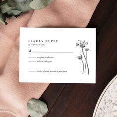 a wedding response card on top of a table with flowers and greenery next to it