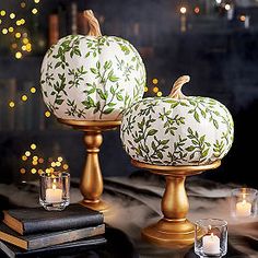 two white pumpkins sitting on top of gold candlesticks next to each other