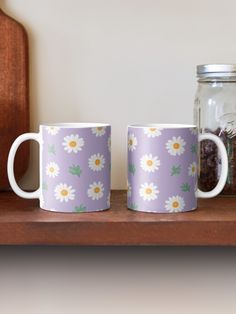 two coffee mugs sitting on top of a wooden shelf next to a glass jar