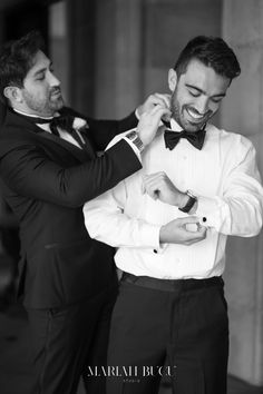 two men in tuxedos helping each other adjust their bow tie