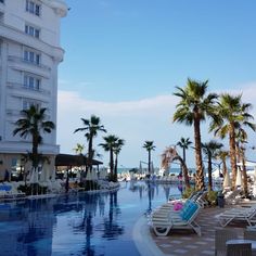 an empty swimming pool with lounge chairs and palm trees