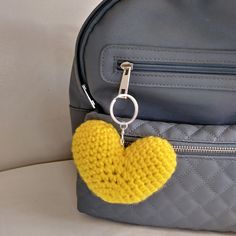 a yellow heart shaped keychain hanging from a gray backpack on a white couch