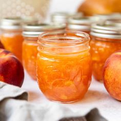 several jars filled with peach jam sitting next to two apples on a white table cloth