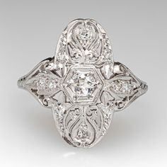 This lovely circa 1910s diamond ring features a pierced design with engraved details and bordered with milgrain edging. The ring is centered with one (1) old European cut diamond bead set into a hexagonal shaped setting. The gallery is also accented with ten (10), bead set, round single cut diamonds. The ring measures 20.2mm at the top, rises 5.8mm above the finger, tapering to 1.4mm wide and 0.9mm thick at the base of the shank. "1916" is engraved on the inside shank. It is currently a size 9.7 Victorian Style White Diamond Ring, Victorian Style Diamond White Diamond Ring, Victorian Diamond White Diamond Ring, Victorian White Diamond Ring In Platinum, Victorian White Diamond Ring With Accents, White Victorian Diamond Ring With Accents, Victorian White Diamond Platinum Ring, Victorian Style White Diamond Platinum Ring, Classic Octagon Diamond Ring With Accents