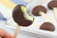 a person holding a chocolate covered dessert on a stick with matchsticks next to it