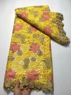 a hand is holding up a yellow and pink lace with flowers on the edge,