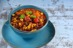 a blue bowl filled with chili and corn on top of a saucer next to a spoon