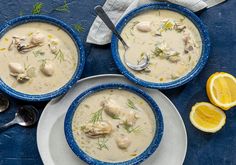 three bowls filled with soup next to lemon slices and spoons on a blue table