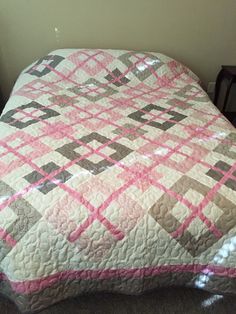 a bed with a pink and gray quilt on it