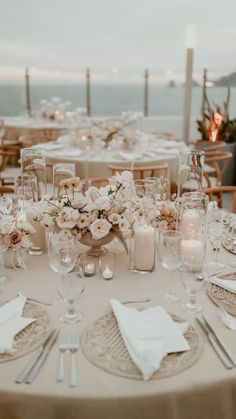 the table is set with white flowers and candles for an elegant wedding reception at the beach