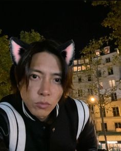 a man with cat ears on his head sitting in front of a building at night