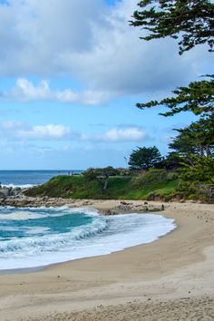 a sandy beach next to the ocean under a cloudy blue sky