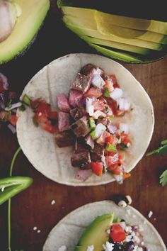 two tortillas with meat and vegetables on them next to sliced avocado