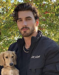 a man holding a dog in his arms and wearing a black jacket with white lettering on it