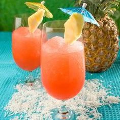 two glasses filled with drinks sitting on top of a blue table cloth next to a pineapple