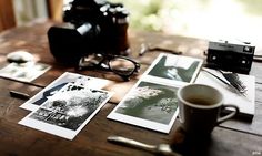 a table topped with pictures and a camera next to a cup of coffee on top of a wooden table