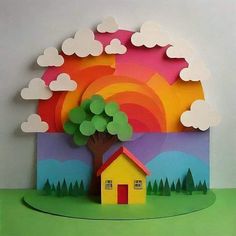 a paper cut out of a house with trees and clouds in the background on a green surface