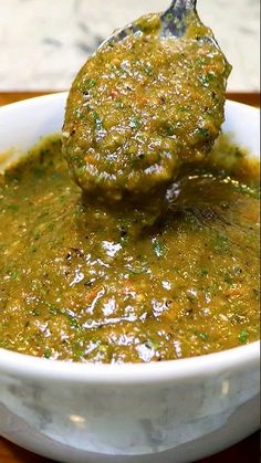 a spoon full of green sauce on top of a white bowl