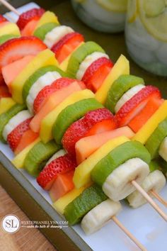 fruit skewers are lined up on a white plate with strawberries and melon