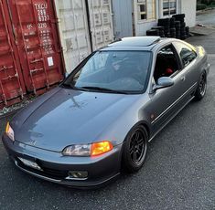 a gray car parked in front of some shipping containers on the side of the road