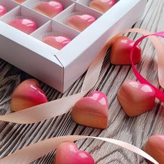 some heart shaped chocolates in a box on a wooden table next to ribbons and ribbon