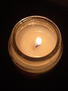 a lit candle in a glass jar on a dark surface with only one light visible