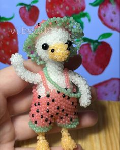 a person holding a small beaded bird in their hand with strawberries on the background