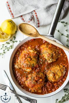 a white bowl filled with meatballs covered in sauce and garnished with herbs