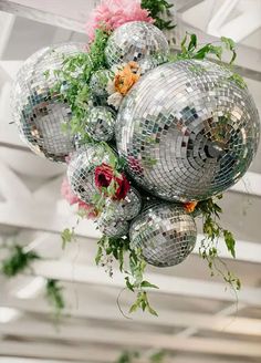 a bunch of disco balls hanging from the ceiling with flowers and greenery around them