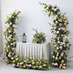 a table topped with flowers and greenery next to a white wall covered in vines