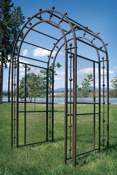 an iron garden arbor with birds on it in a grassy area next to the water