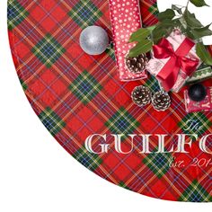 a red and green plaid table cloth with presents on it, pine cones, balls, and holly leaves