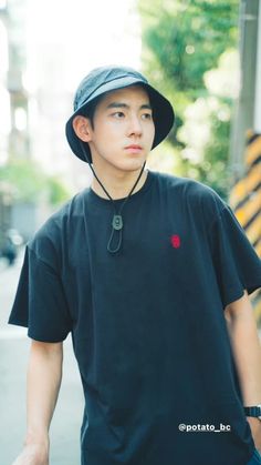 a young man wearing a hat and black shirt is walking down the street with his hand in his pocket