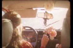 a woman sitting in the driver's seat of a car with flowers on her lap