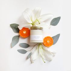 an orange and white flower next to a jar filled with some kind of candle on top of a table