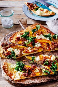 a pizza with cheese, spinach and other toppings on a wooden cutting board