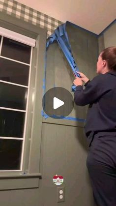 a woman is painting the wall with blue tape