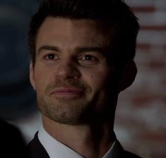 a close up of a person wearing a suit and tie with a brick wall in the background