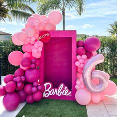 there is a pink frame with balloons and the number six on it in front of some palm trees