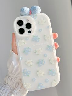 a person holding an iphone case with flowers on it and two small blue pom poms attached to the back