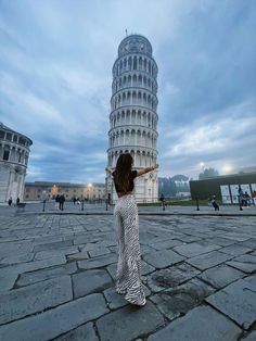 a woman standing in front of the leaning tower of pisa with her arms spread out