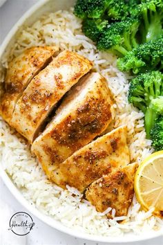 chicken breast, rice and broccoli on a white plate with lemon wedges