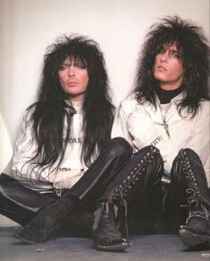 two people sitting on the ground with long hair and leather pants, one wearing black boots