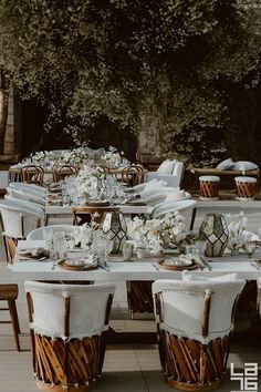 an outdoor dining area with tables and chairs covered in white linens, surrounded by greenery