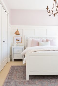 a white bed sitting in a bedroom next to a dresser and a chandelier