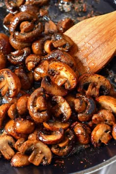 mushrooms being cooked in a skillet with a wooden spoon