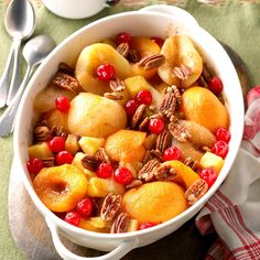 a white bowl filled with fruit and nuts on top of a wooden table next to silverware